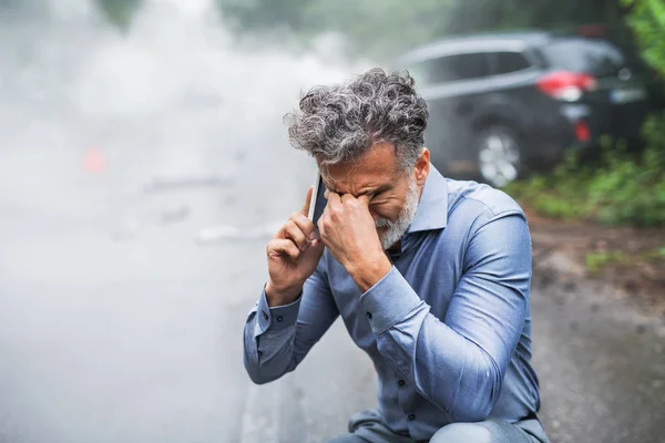 Homme mûr passer un coup de fil après un accident de voiture, fumée en arrière-plan . — Photo