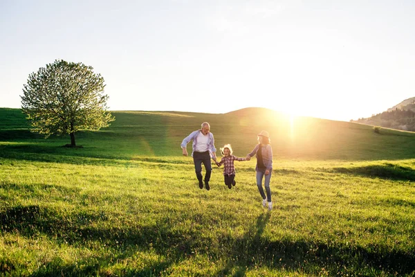 Senior couple with granddaughter on a walk outside in spring nature, jumping. — Stock Photo, Image