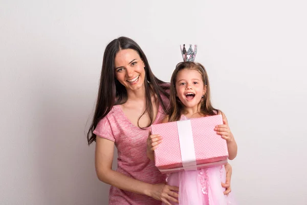 Uma menina pequena com cabeça de coroa e sua mãe segurando um presente em um estúdio . — Fotografia de Stock