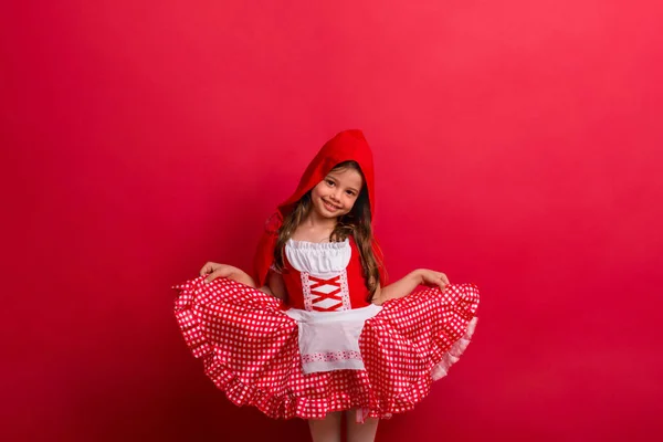 Una bambina in costume Cappuccetto Rosso in studio su sfondo rosso . — Foto Stock