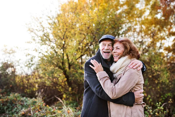 Äldre par stående i en höst natur, kramas. — Stockfoto