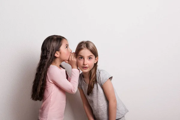 Una niña pequeña susurrando algo en un oído de su amigo . —  Fotos de Stock