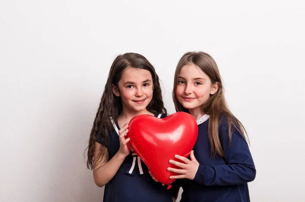 To små piger i et studie, der holder en rød hjerte ballon foran dem . - Stock-foto