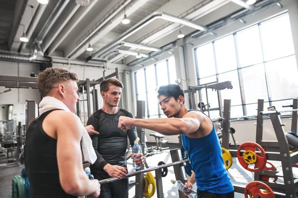 Jóvenes amigos de pie y hablando en el moderno gimnasio crossfit, sosteniendo botellas de plástico . —  Fotos de Stock