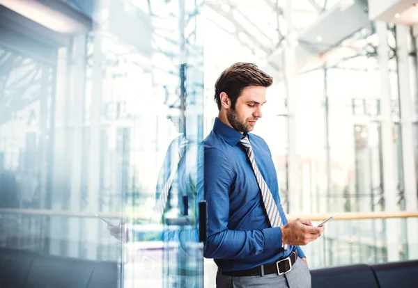 En ung affärsman med smartphone stående i en modern byggnad, textning. — Stockfoto