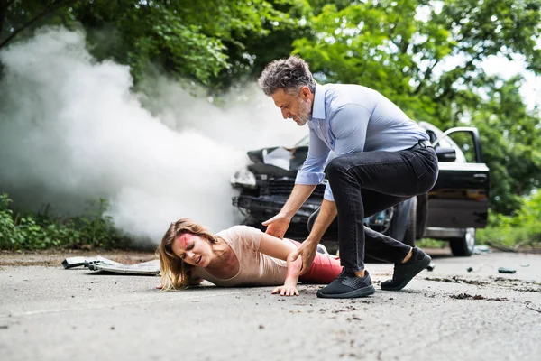 A man helping a young woman lying on the road after a car accident. — Stock Photo, Image