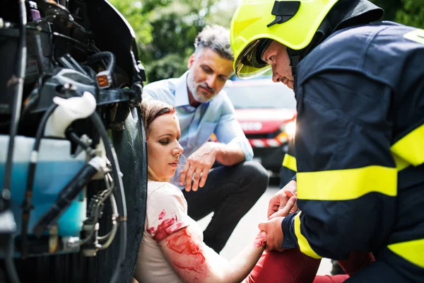 Un pompier ajuta o tanara ranita care sta langa masina pe un drum dupa un accident . — Fotografie, imagine de stoc