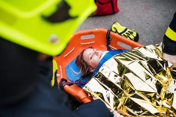 Uma mulher ferida em uma maca de plástico após um acidente de carro, coberta por cobertor térmico . — Fotografia de Stock