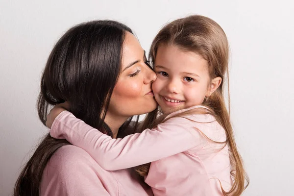 En närbild av en ung mamma kysser hennes lilla dotter i en studio. — Stockfoto