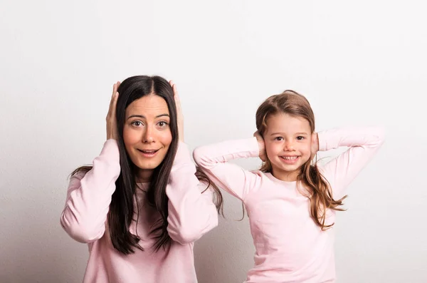 Uma menina pequena e sua mãe em um estúdio, tapando os ouvidos com as mãos . — Fotografia de Stock