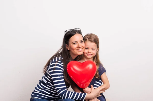 En liten flicka och hennes mamma håller ett rött hjärta i en studio. — Stockfoto