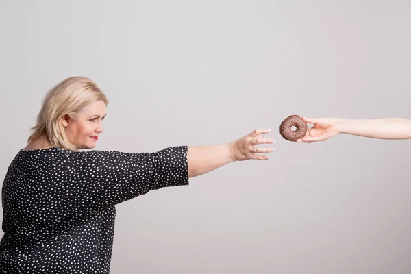 Eine glückliche übergewichtige Frau im Studio, die nach einem Donut greift. — Stockfoto