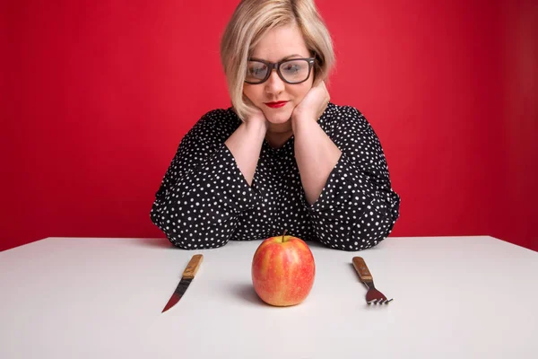 Portrait of an attractive overweight woman in studio, looking at an apple on the table. — Stock Photo, Image