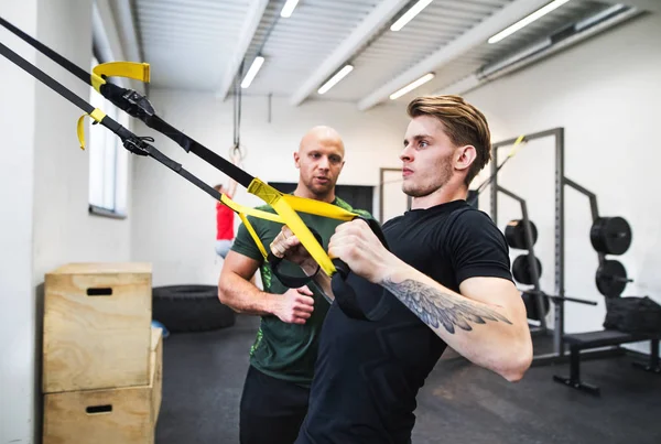 Passar ung man med en personlig tränare i gymmet som gör träning med Trx. — Stockfoto