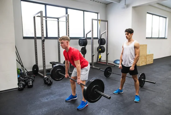 Ajustar a los hombres jóvenes en el gimnasio de entrenamiento, levantando la barra . —  Fotos de Stock