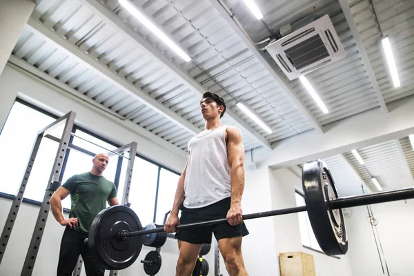 Fit pemuda dengan pelatih pribadi di gym bekerja, mengangkat barbel . — Stok Foto