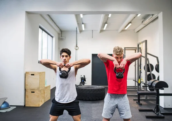 Två unga män i gymmet gör kettlebell gungor. — Stockfoto