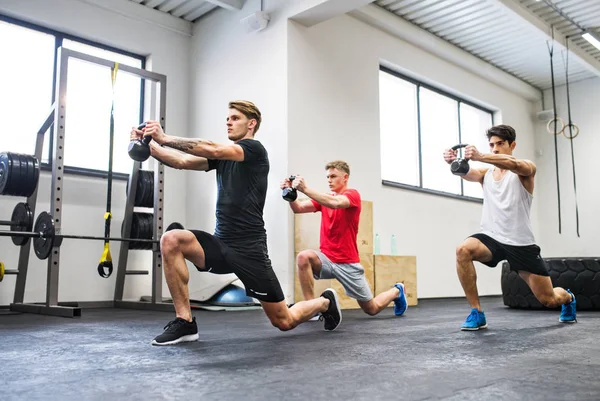 Tre unga män i gymmet som gör träning med kettlebells. — Stockfoto