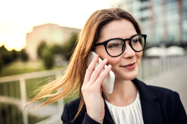 Una joven mujer de negocios con smartphone al aire libre, haciendo una llamada telefónica . — Foto de Stock