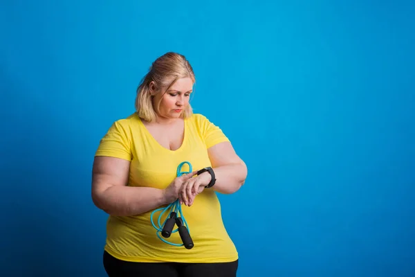 Ritratto di una felice donna sovrappeso con smartwatch e corda da salto in studio . — Foto Stock