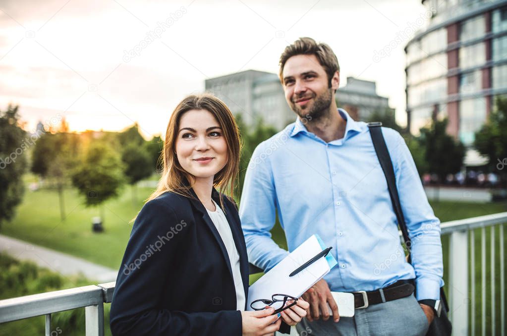 A young businessman and businesswoman standing on a bridge.