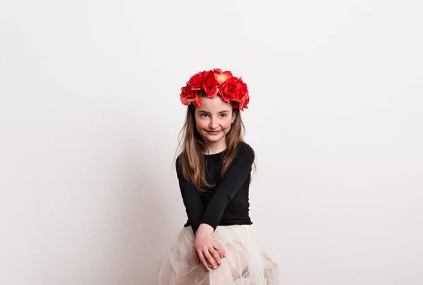 En liten flicka med blomma headband sitter i en studio, händerna på knä. — Stockfoto
