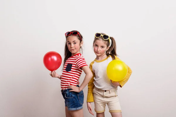 Chicas pequeñas con gafas de sol y globos de pie en un estudio . — Foto de Stock