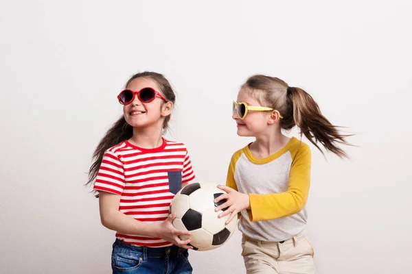 Små flickor med solglasögon och en fotboll bollen stå i en studio. — Stockfoto