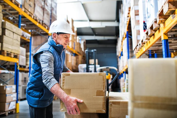 Senior mannelijke magazijn werknemer lossen dozen van een pallettruck. — Stockfoto