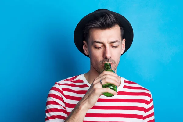Porträt eines jungen Mannes in einem Studio, der aus einer Flasche auf blauem Hintergrund trinkt. — Stockfoto