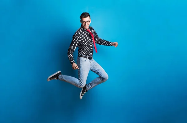 Retrato de un joven con gafas en un estudio sobre fondo azul, saltando . —  Fotos de Stock