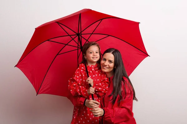 En liten flicka med sin mor under ett parasoll på en vit bakgrund. — Stockfoto