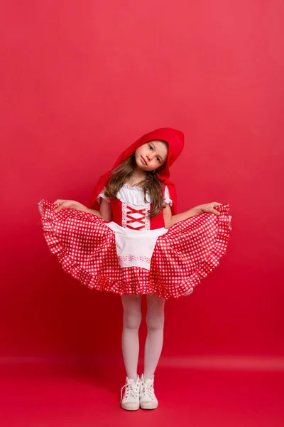 Una bambina in costume Cappuccetto Rosso in studio su sfondo rosso . — Foto Stock