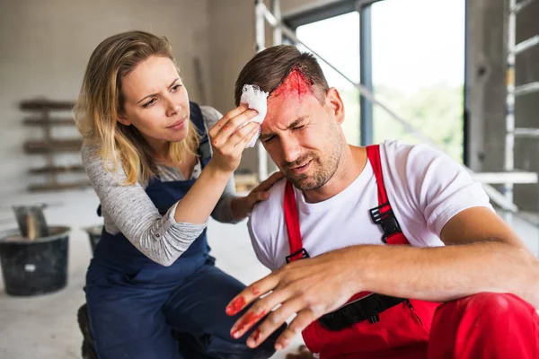 Uma mulher ajudando o homem trabalhador após um acidente no canteiro de obras . — Fotografia de Stock