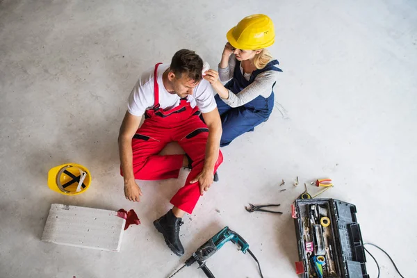 Žena s smartphone pomáhá pracovník muž po nehodě na staveništi. — Stock fotografie