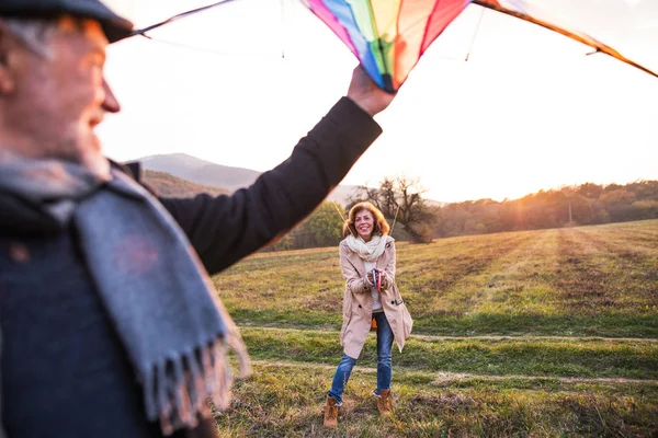 Carefree senior couple flying a kite in an autumn nature at sunset. — Stock Photo, Image