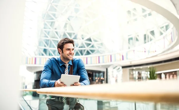 A young businessman with tablet leaning on a railing in a modern building. — Stock Photo, Image