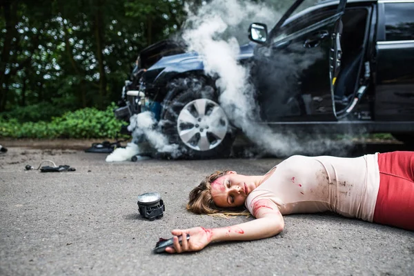 Mujer joven lesionada yaciendo en la carretera después de un accidente de coche, inconsciente . — Foto de Stock