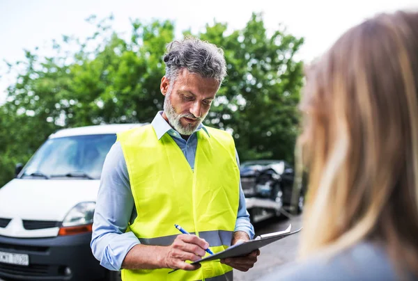 Een verzekeringsagent in gesprek met een vrouw buiten op de weg na een auto-ongeluk. — Stockfoto