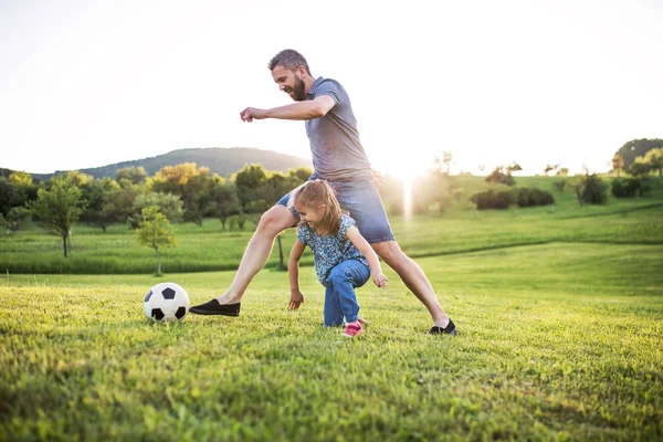 Padre con una pequeña hija jugando con una pelota en la naturaleza de primavera al atardecer . — Foto de Stock