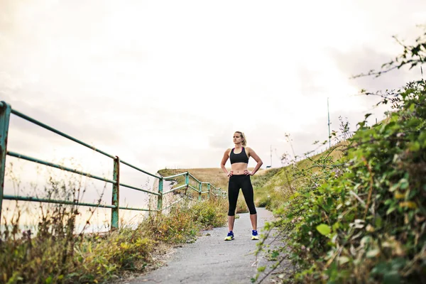 Giovane donna sportiva corridore in activewear nero in piedi fuori nella natura, riposante . — Foto Stock