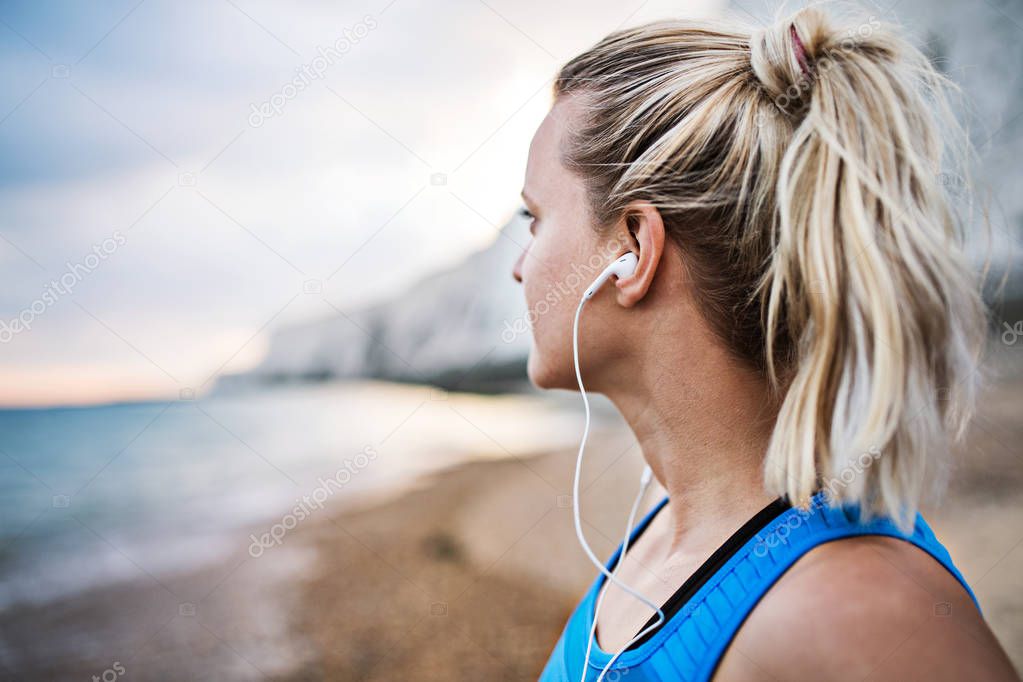 Young sporty woman runner with earphones standing on the beach outside.