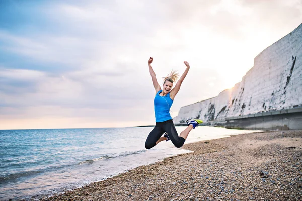 Giovane donna sportiva corridore in blu abbigliamento sportivo saltare sulla spiaggia al di fuori . — Foto Stock