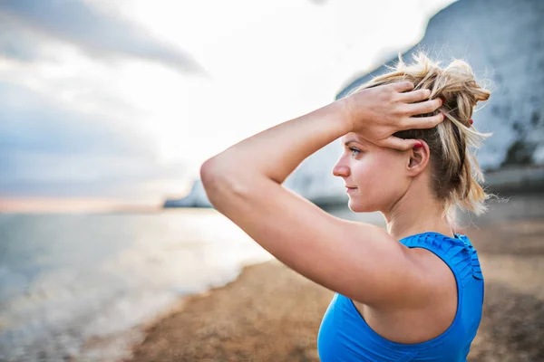Giovane donna sportiva corridore in blu abbigliamento sportivo in piedi sulla spiaggia al di fuori . — Foto Stock