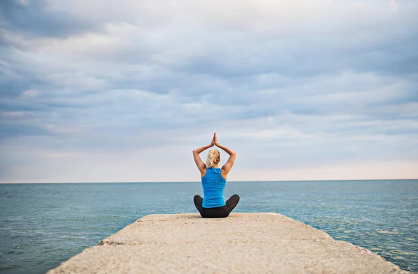 Okyanusun dışında tarafından yoga egzersiz yaparak genç bir sportif kadın arkadan görünüş. — Stok fotoğraf