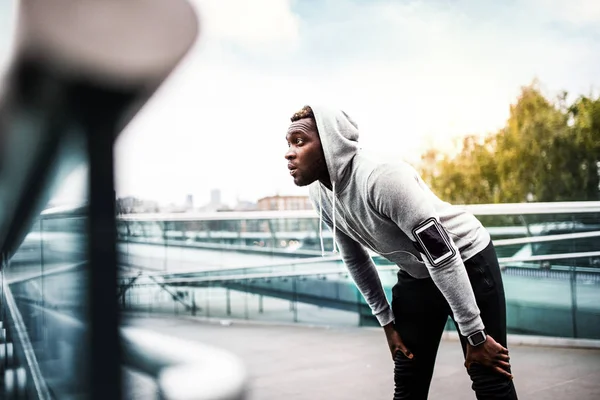 年轻的运动黑色男子赛跑者与智能手机在城市的桥梁, 休息. — 图库照片