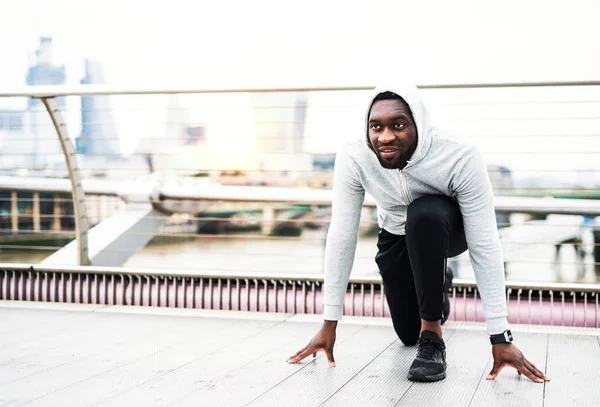 Joven corredor negro deportivo en posición inicial en el puente en una ciudad . —  Fotos de Stock