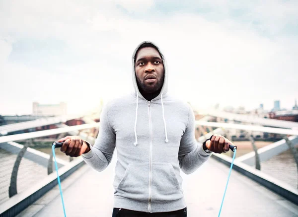 Fiatal active fekete sportoló ugró egy kötéllel a városban, kapucnis visel. — Stock Fotó