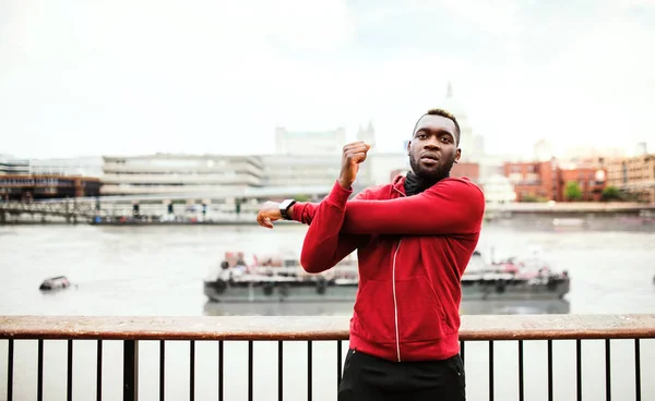 Fiatal sportos fekete férfi futó csinál, stretching a hídon kívül a városban. — Stock Fotó