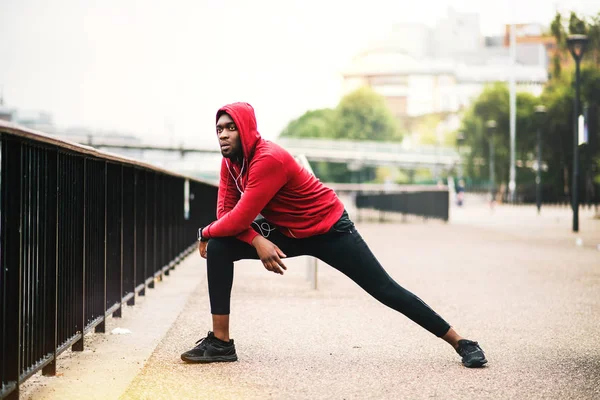 Молодой спортивный чернокожий бегун делает растяжку на мосту в городе . — стоковое фото